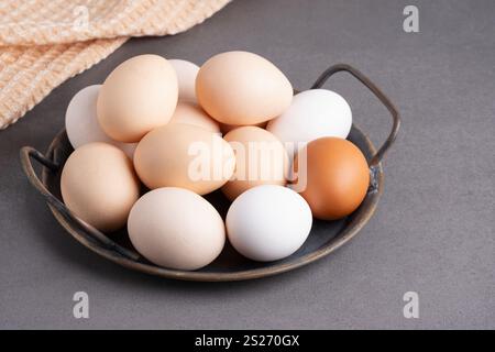 A collection of fresh eggs displayed in a rustic bowl on a textured countertop with a soft cloth in the background. Stock Photo