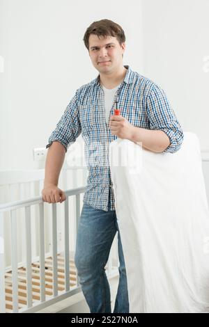 Young expectant father putting mattress in baby's cot Stock Photo