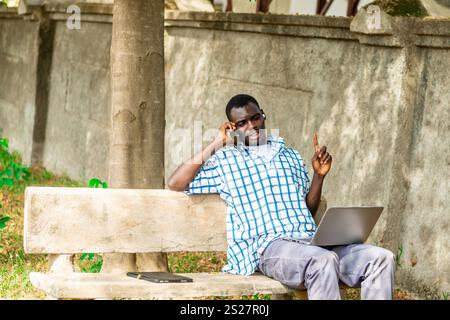 Young cheerful black man using mobile phone and laptop computer. Modern lifestyle Stock Photo