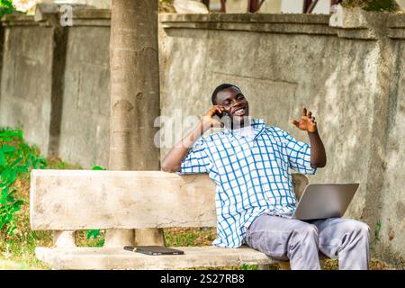Young cheerful black man using mobile phone and laptop computer. Modern lifestyle Stock Photo
