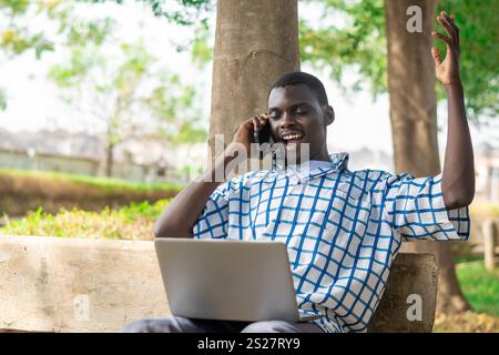 Young cheerful black man using mobile phone and laptop computer. Modern lifestyle Stock Photo