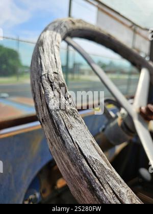 A close-up view of a weathered wooden steering wheel shows the aging wood and the metal center. Stock Photo