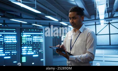 Engineer walking in data center, monitoring security threats, implementing cybersecurity measures. Indian man ensuring compliance with regulations to protect data center gear, camera B Stock Photo