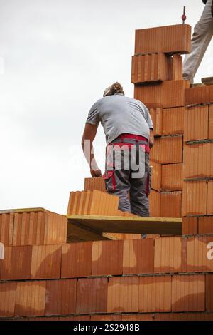 Anonymous construction worker on a building site erecting a brick wall. Brick wall of a solid house. Symbolic image of illegal labour and bungling Aus Stock Photo
