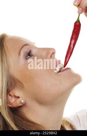 A young woman bites into a chilli pepper. Against a white background Austria Stock Photo