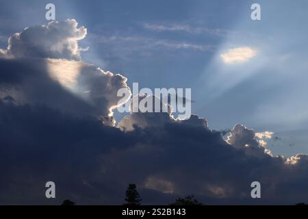 streaks of sunlight blaze out from behind gray clouds at sunset Stock Photo