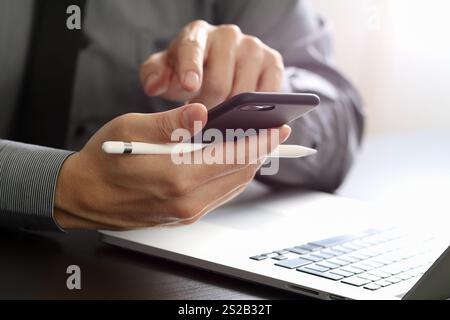 close up of businessman working with mobile phone and stylus pen and laptop computer on wooden desk in modern office Stock Photo