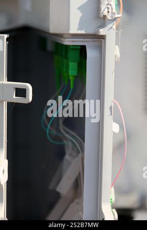 Interconnected wires in green and clear plastic casings are visible through an open utility box at a construction site, bathed in bright sunlight, ind Stock Photo