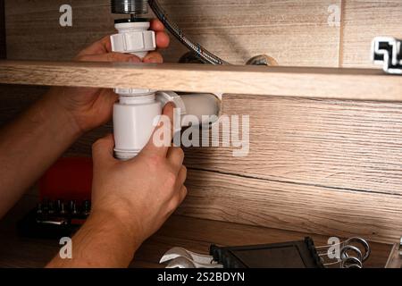 Plumber working on sink drain pipe installation in bathroom, using pvc pipes and connectors. Stock Photo