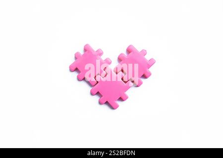 Three pink puzzle pieces arranged together in the shape of a heart on a white background Stock Photo