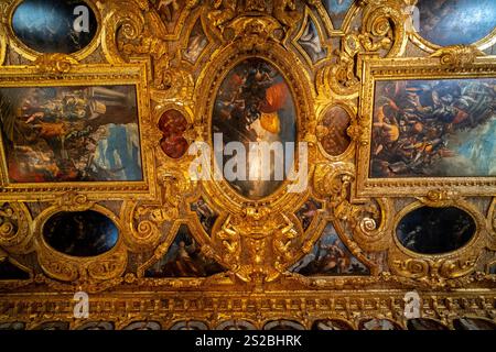 An opulent ceiling featuring elaborate gold frames and detailed frescoes depicting dramatic battle scenes, mythological figures, and allegorical theme Stock Photo