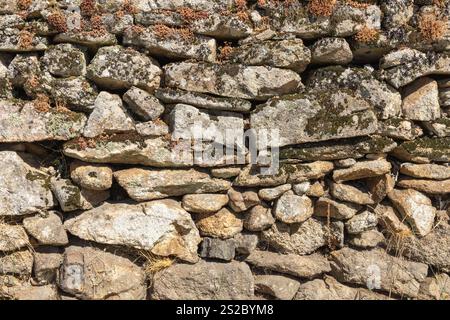 Detail of a granite wall with moss, large and small gray stones stacked on top of each other part of an old historic Portuguese house. Stock Photo