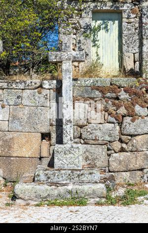 Religious granite christianity cross in font of granite wall with moss in a street of Quintela Portugal. Stock Photo