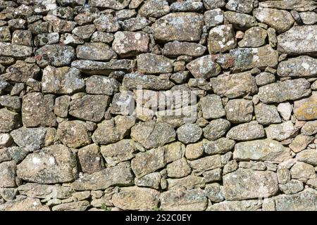 Detail of a granite wall with moss, large and small gray stones stacked on top of each other part of an old historic house Stock Photo