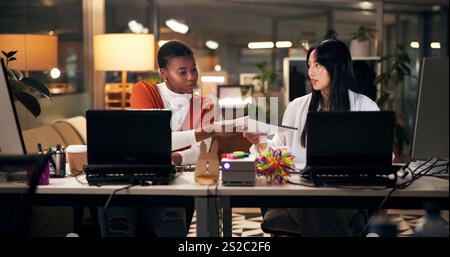 Business women, documents or night with laptop for project report, review or web design at office. Female people, designers or colleagues working late Stock Photo