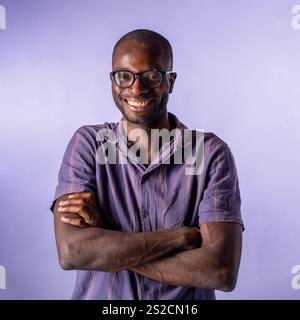African man smiling confidently with crossed arms in a studio portrait with a pastel purple background Stock Photo