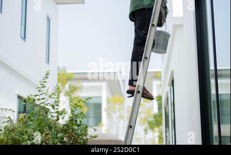 Cropped shot of painter man at work with a roller, bucket and ladder, bottom view. Bucket to renovation, construction concept. Stock Photo