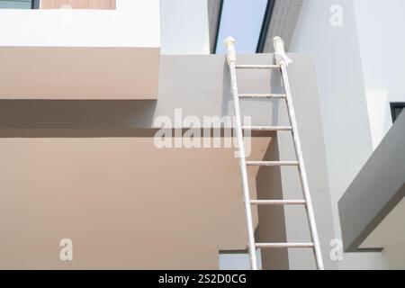 Metallic folding ladder near beige wall outdoors during house renovation. Copy space. Stock Photo