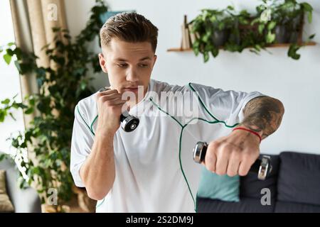 Young man trains indoors, lifting dumbbells with a determined focus on fitness. Stock Photo