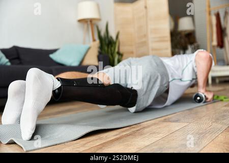Young man with a prosthetic leg shows dedication while doing push ups on a yoga mat indoors. Stock Photo