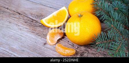 Juicy oranges and tangerine slices are arranged on a weathered wooden surface with pine branches, suggesting a fresh, natural ambiance. Stock Photo
