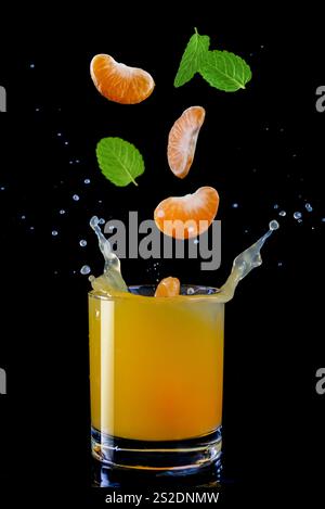 A vibrant citrus drink splashes as tangerine slices and mint leaves create lively droplets against a dark backdrop. Stock Photo
