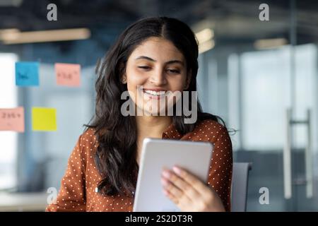 Businesswoman using tablet computer at work inside office. Smiling woman using app and reading electronic report. Stock Photo