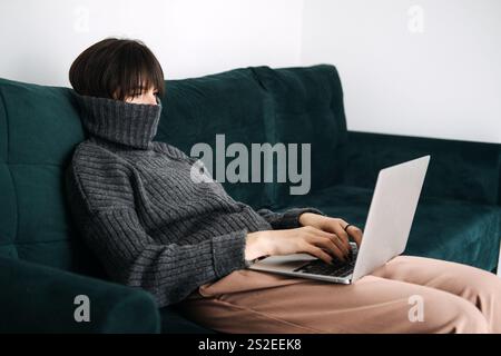 Woman working remotely on laptop, cozy work-from-home setup, mental health and well-being, balancing productivity, home office comfort, self-care. Stock Photo
