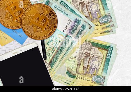 1000 Sri Lankan rupees bills and golden bitcoins with smartphone and credit cards. Cryptocurrency investment concept. Crypto mining or trading transac Stock Photo