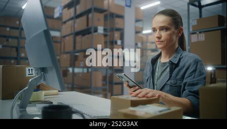Female inventory clerk scans parcel using smartphone, enters data on computer, works with E-commerce online orders. Sorting center worker checking boxes for delivery. Warehouse of delivery service. Stock Photo
