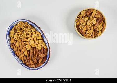 Assorted nuts in a stoneware container with a straw basket, on a white background. Almonds, Walnuts, Cashews and Chestnuts Stock Photo