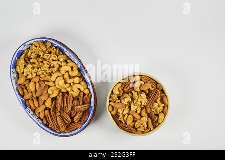 Assorted nuts in a stoneware container with a straw basket, on a white background. Almonds, Walnuts, Cashews and Chestnuts Stock Photo