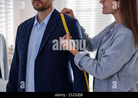 Tailor measuring jacket on man during fitting in atelier, closeup Stock Photo