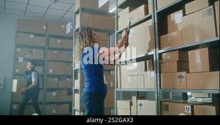 Female inventory manager walks with colleague, uses tablet computer. African American warehouse worker puts parcel on the shelf. Team of multiethnic employees working in logistics distribution center. Stock Photo
