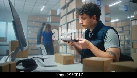 Male warehouse clerk scans parcels for delivery using tablet computer, works in postal service or online store logistics storage. Sorting center employees carrying cardboard boxes. E-commerce products Stock Photo