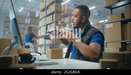 African American warehouse clerk scans parcels using tablet computer, works in post office. Sorting center employees carrying cardboard boxes for shipping. Logistics storage with online store products Stock Photo