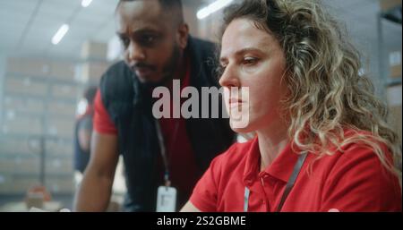 Two diverse warehouse workers or logistics specialists talking, preparing E-commerce orders for shipping to customers, using laptop computer, working in post office. Online store delivery service. Stock Photo