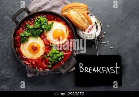 Shakshuka eggs in a pans with bread on a dark background. Poached eggs in a spicy tomato pepper sauce. Traditional Jewish scrambled eggs. Top view. Stock Photo