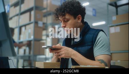 Logistics manager scans small parcels using smartphone, works in warehouse of post office. Sorting center workers carrying cardboard boxes for delivery to customers. Storage with E-commerce orders. Stock Photo