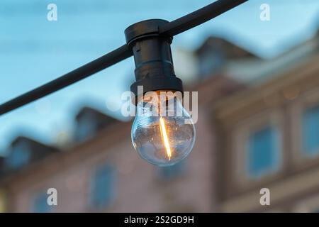 Close-up of a glowing filament light bulb hanging from a black cord. Light bulb garland Stock Photo