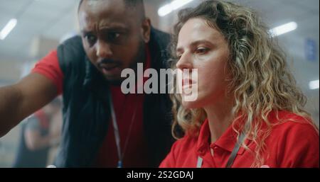 Team of multiethnic warehouse associates or logistics managers talking, preparing E-commerce orders for shipping to clients, using laptop to check inventory. Distribution center or delivery service. Stock Photo