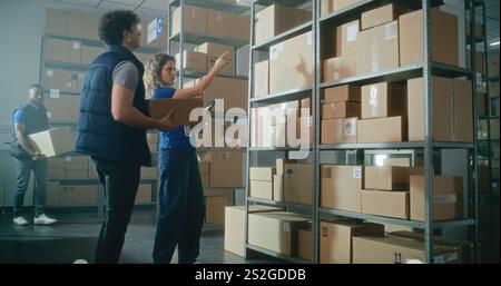 Male warehouse associate puts cardboard box with goods on the shelf. Female inventory manager uses tablet computer, scans code on parcel. Logistics distribution center with E-commerce online orders. Stock Photo