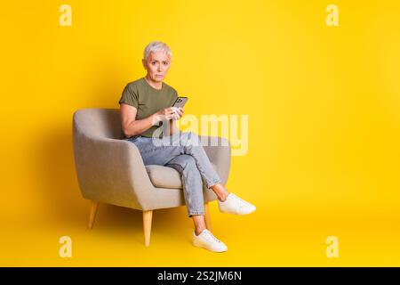 Full length photo of charming sad woman wear khaki t-shirt typing sms modern device empty space isolated yellow color background Stock Photo
