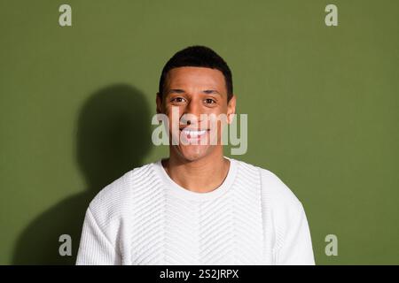 Confident young man smiling against khaki background wearing stylish white sweater Stock Photo