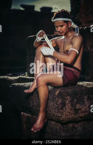 The boxer sat on the stone, tied the tape around his hand, preparing to fight. Stock Photo