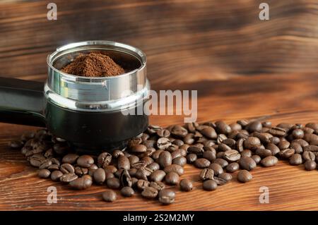 Coffee machine horn with ground coffee. Coffee beans scattered on wooden table. Background with coffee. Stock Photo