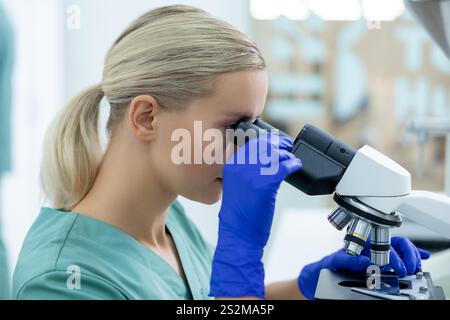 Medical woman wearing gloves working in sterile laboratory using microscope and optical tools Stock Photo