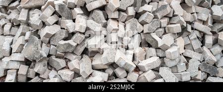 A close-up view of a pile of gray concrete bricks, unevenly stacked and scattered. The bricks vary in shape and size, creating a textured surface. Stock Photo