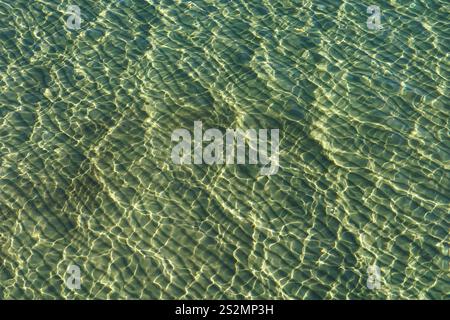 Turquoise sea surface with sand under the water and sun flares in the shallows Stock Photo
