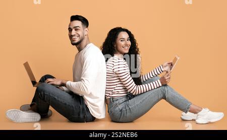 Cheerful arab couple sitting back to back with laptop and digital tablet Stock Photo